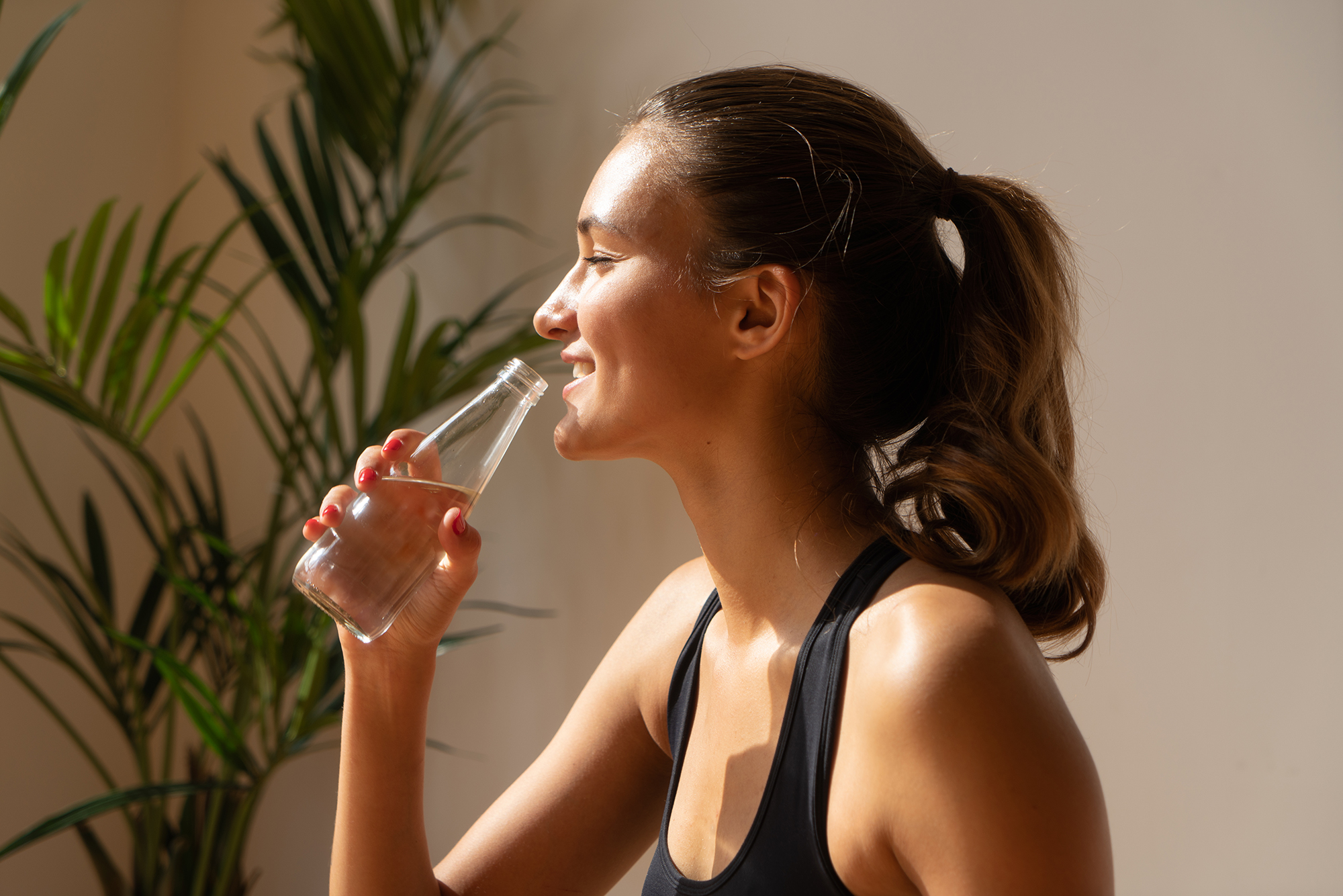 close up portait of sportswoman smiling, drinking water from bottle, natural light